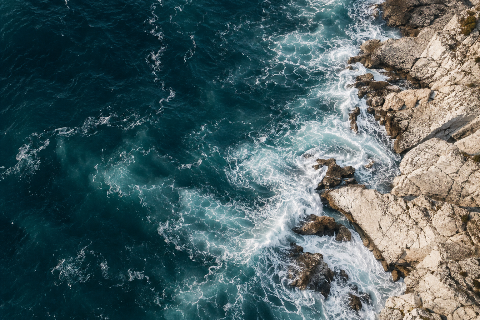 Deep blue ocean waves meeting a sunlit rocky coastline